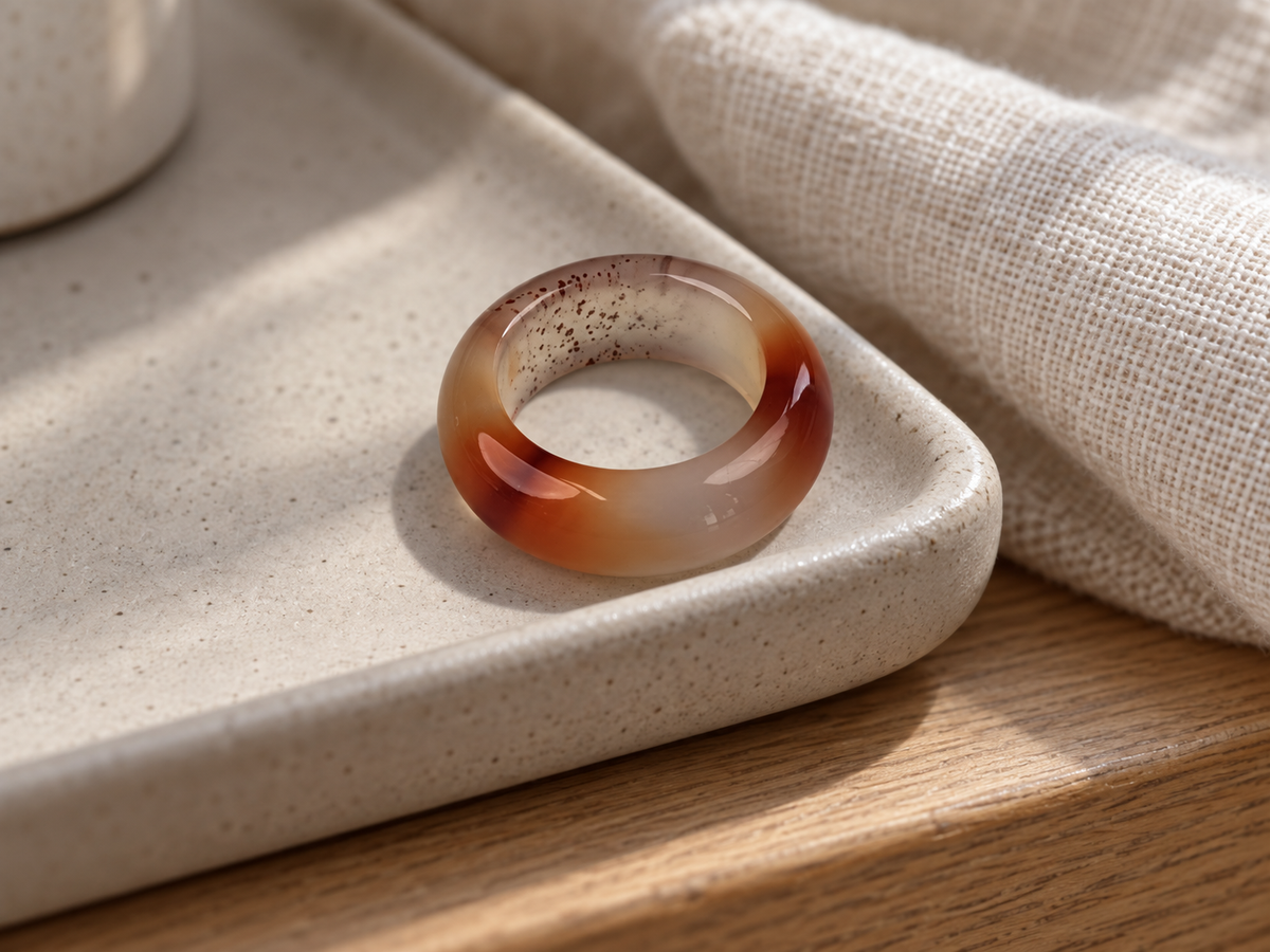 Red and white agate band ring on a ceramic jewelry dish beside linen.