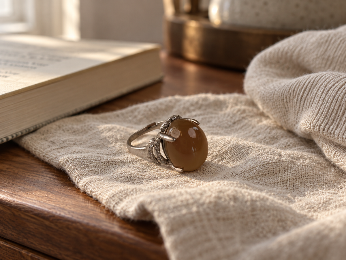 Brown agate claw-set ring resting on linen on a wooden dresser.